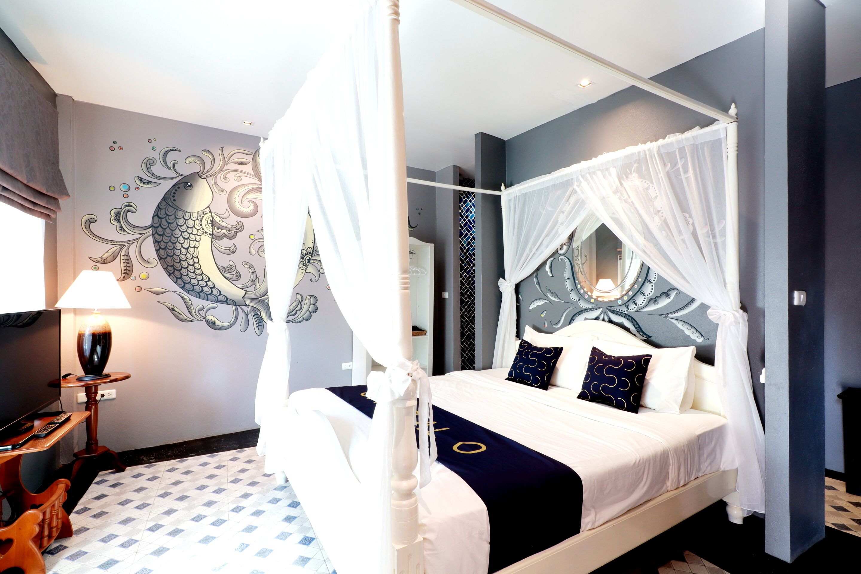 A four-poster canopy bed with a white bedspread and navy blue accent pillows, a decorative wall mural, and a patterned floor.