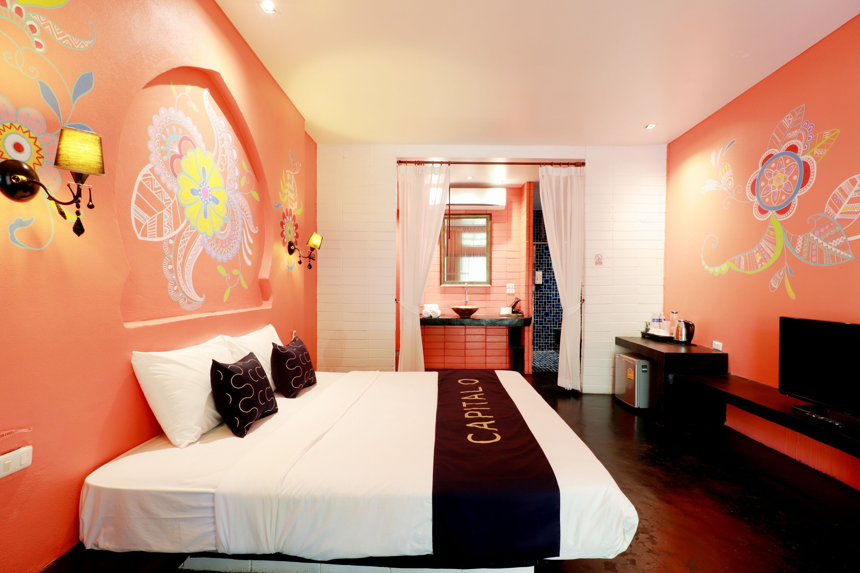 A hotel room with a bed, a TV, a desk, and a bathroom visible through a doorway.