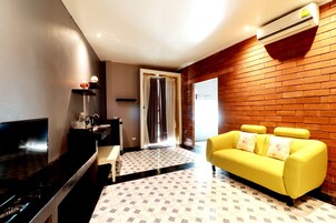 Una sala de estar con televisor, sofá amarillo, mesa de centro y piso estampado.