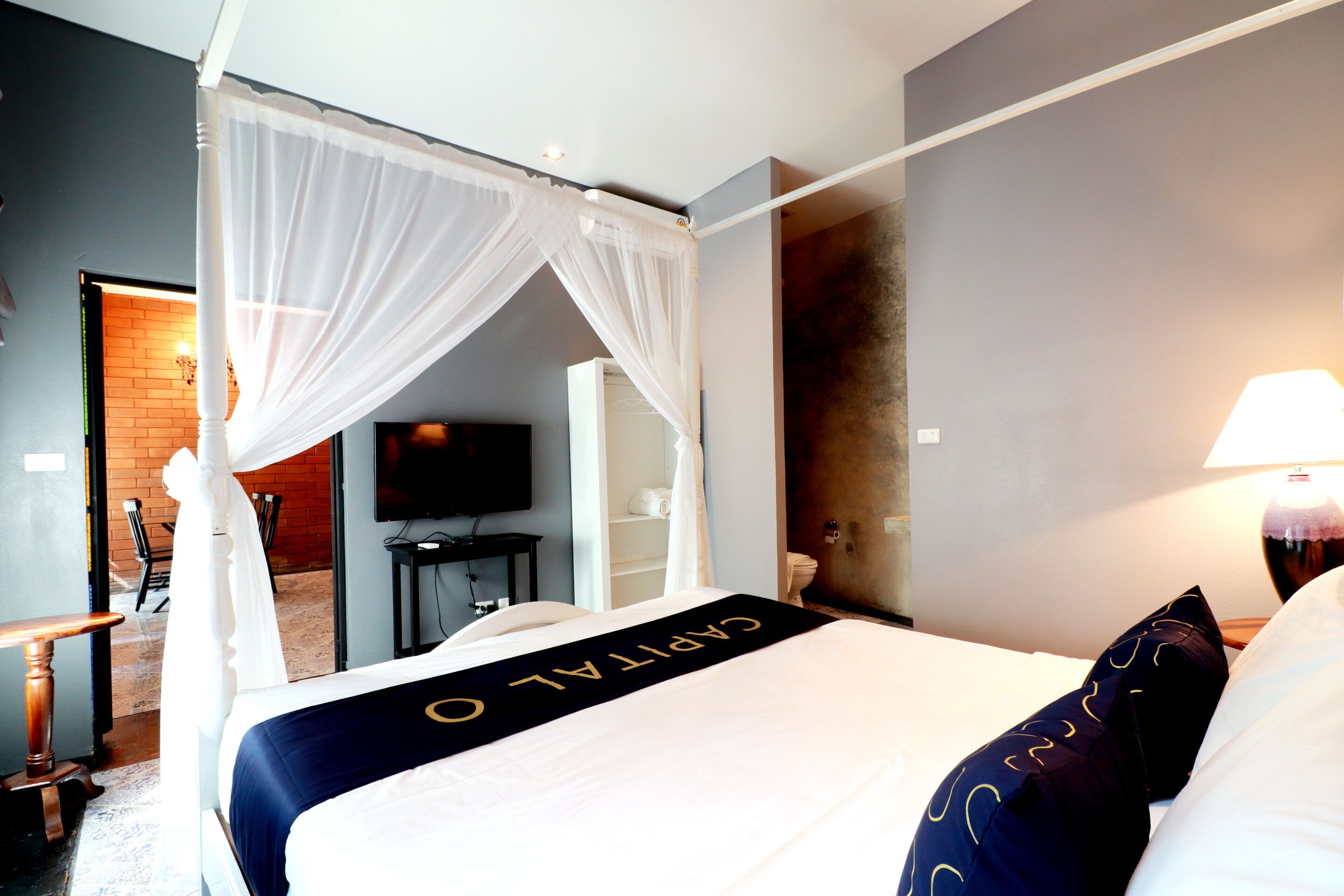 Quarto de hotel com cama, televisão, escrivaninha e banheiro visível através de uma porta aberta.