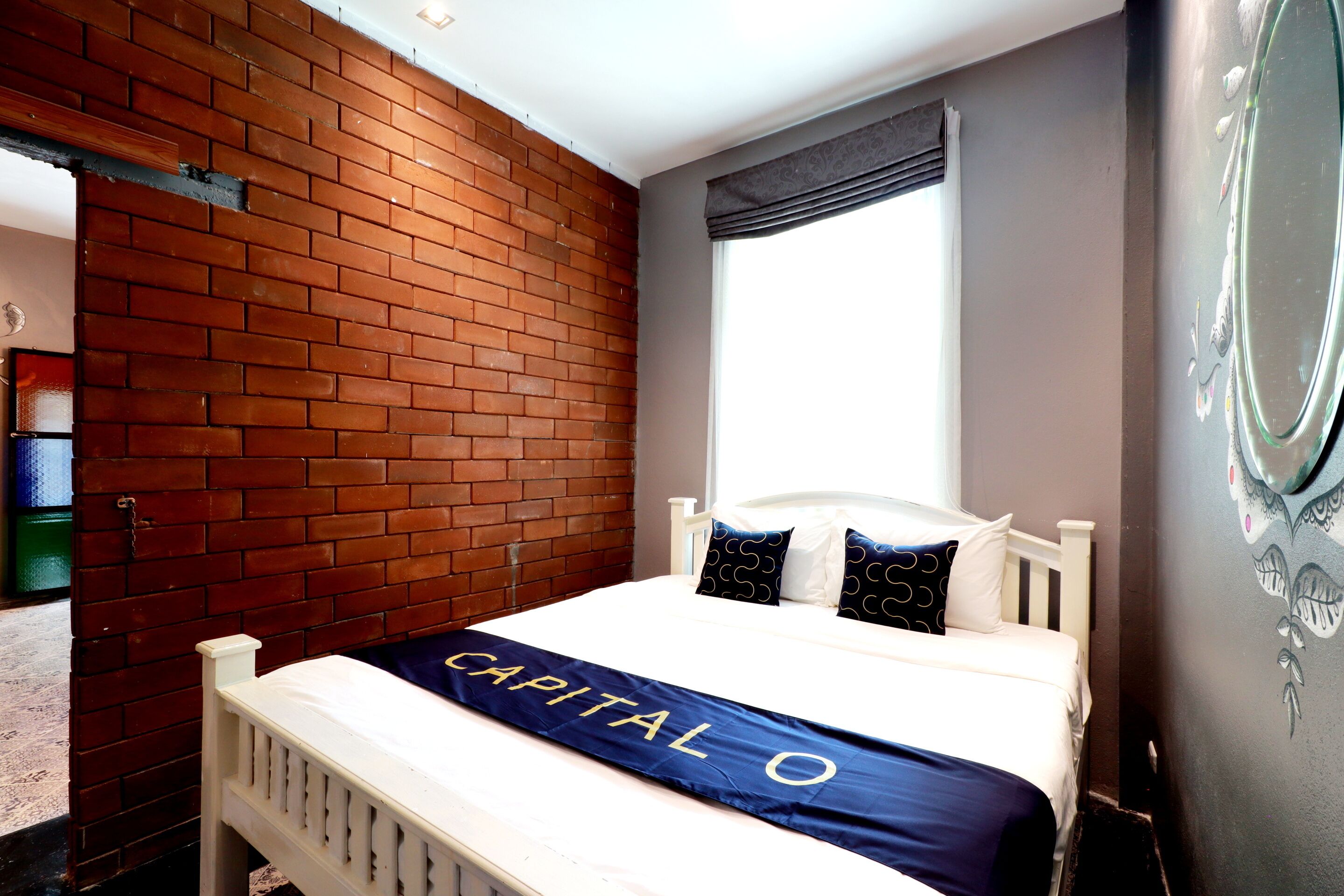 A hotel room with a brick wall, a bed with a blue bedspread, and a window with a curtain.