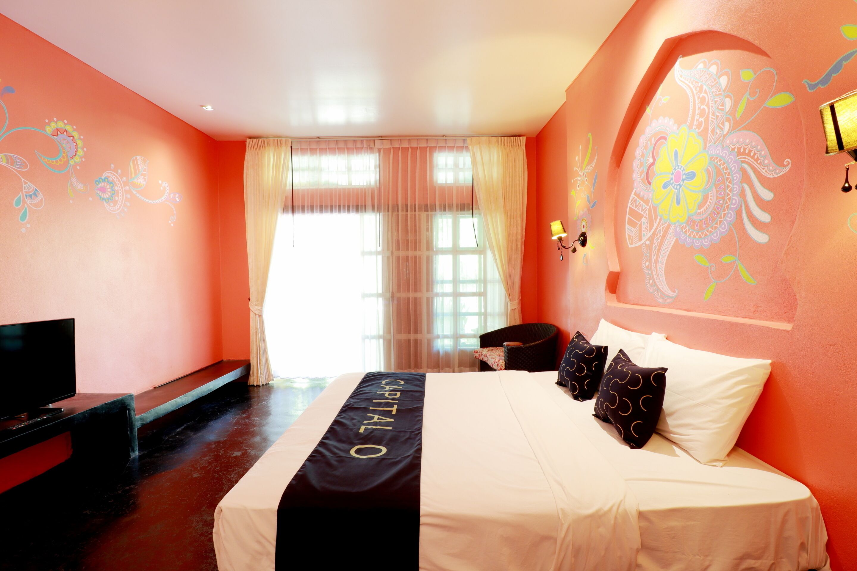 A hotel room with a bed, a TV, and a window with curtains.