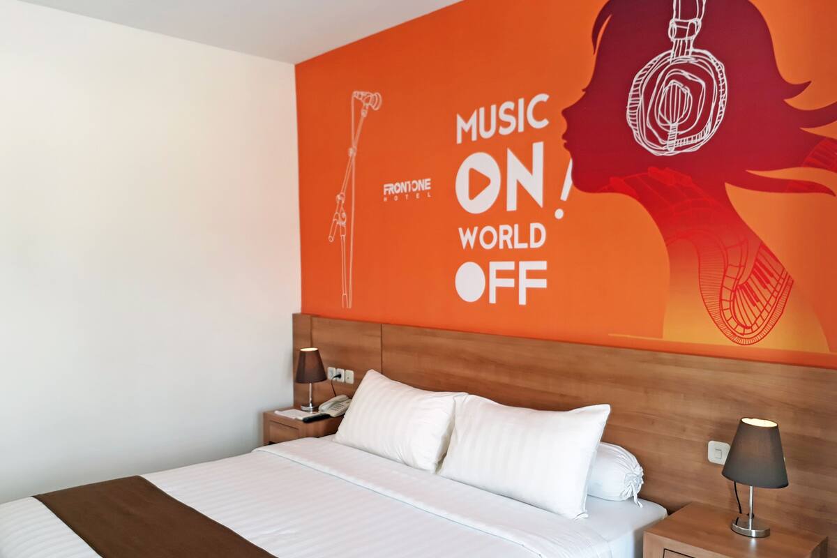Una habitació d'hotel amb un llit, una tauleta de nit, una làmpada i una paret amb un cartell.