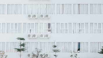 A modern building with multiple floors, large windows with curtains, outdoor seating with umbrellas, and air conditioning units.