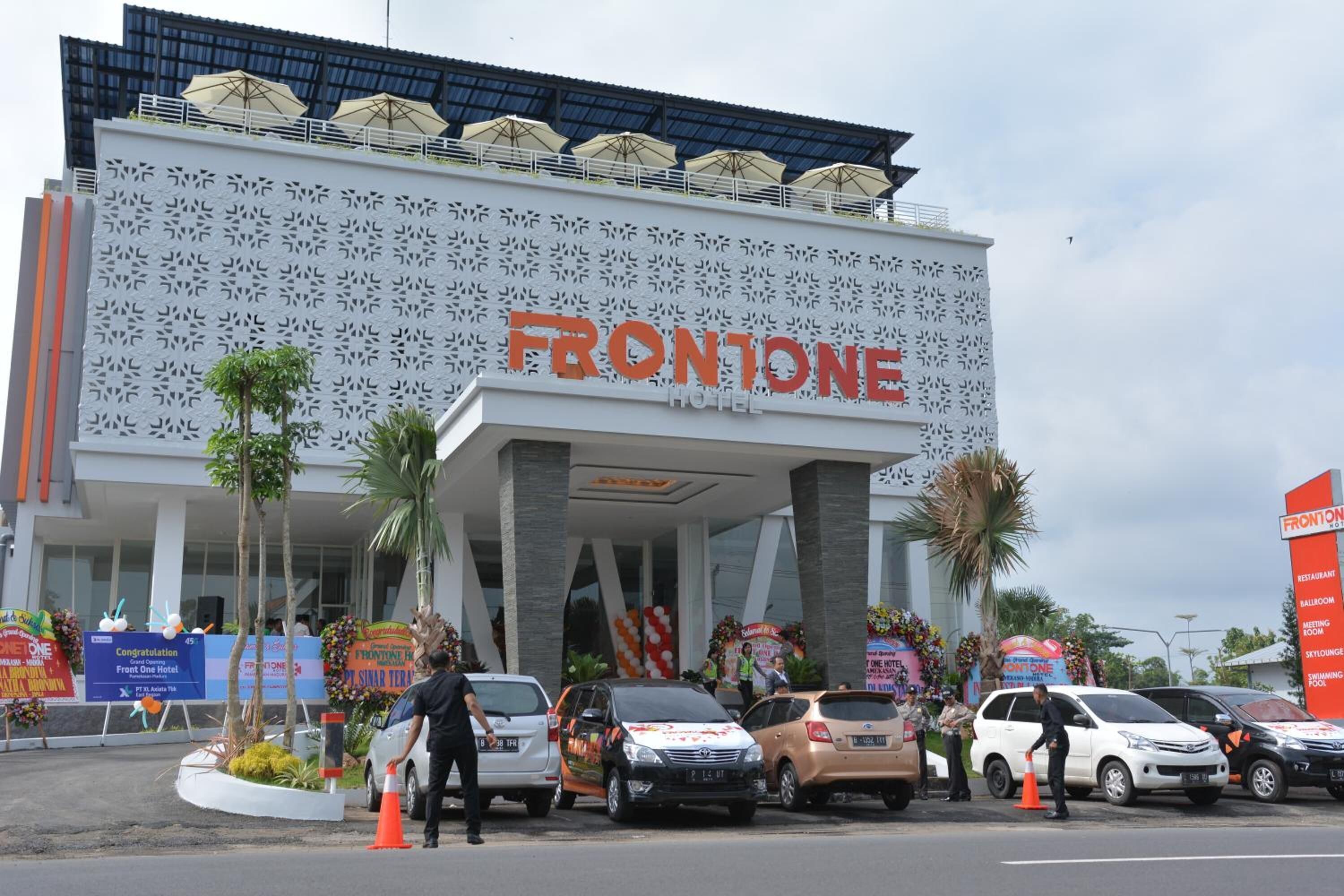 Exterior del Hotel Frontone, con fachada moderna, amplio acceso y varios autos estacionados frente al hotel.