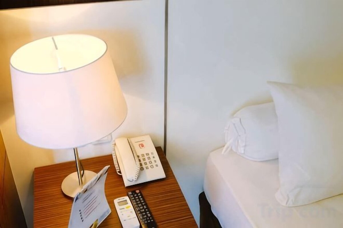 A hotel room with a bedside table, a lamp, a telephone, and a bed with pillows.