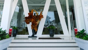 Una entrada moderna a un edificio con fachada de vidrio, una gran escultura decorativa y plantas en macetas.