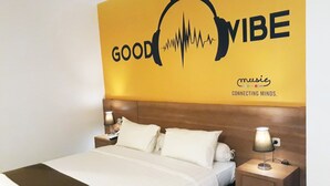 Una habitación de hotel con una cama, una mesita de noche, una lámpara y una pared con un diseño que dice 'GOOD VIBE'.
