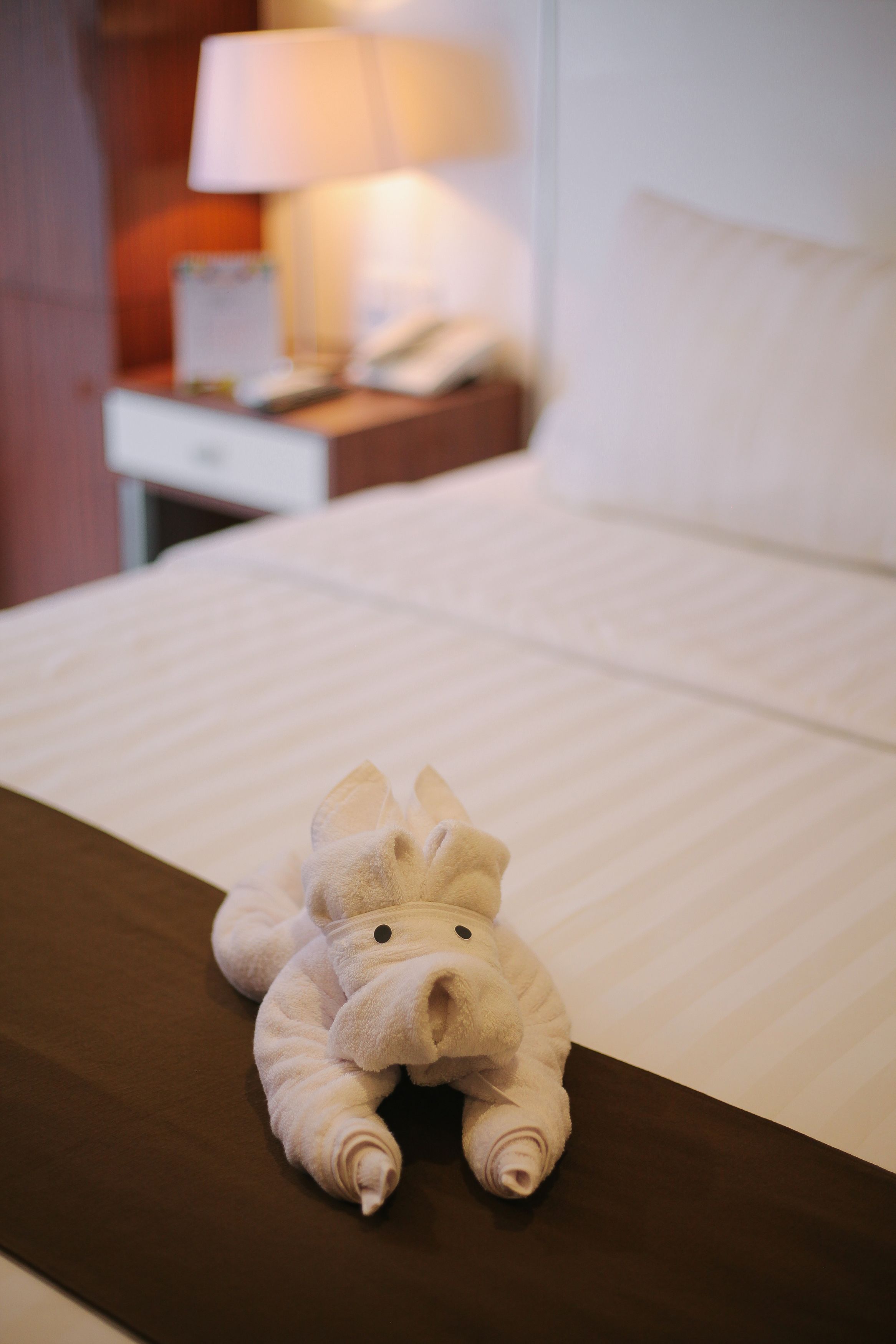 A bed with a plush toy on it, a lamp, and a nightstand with a phone.