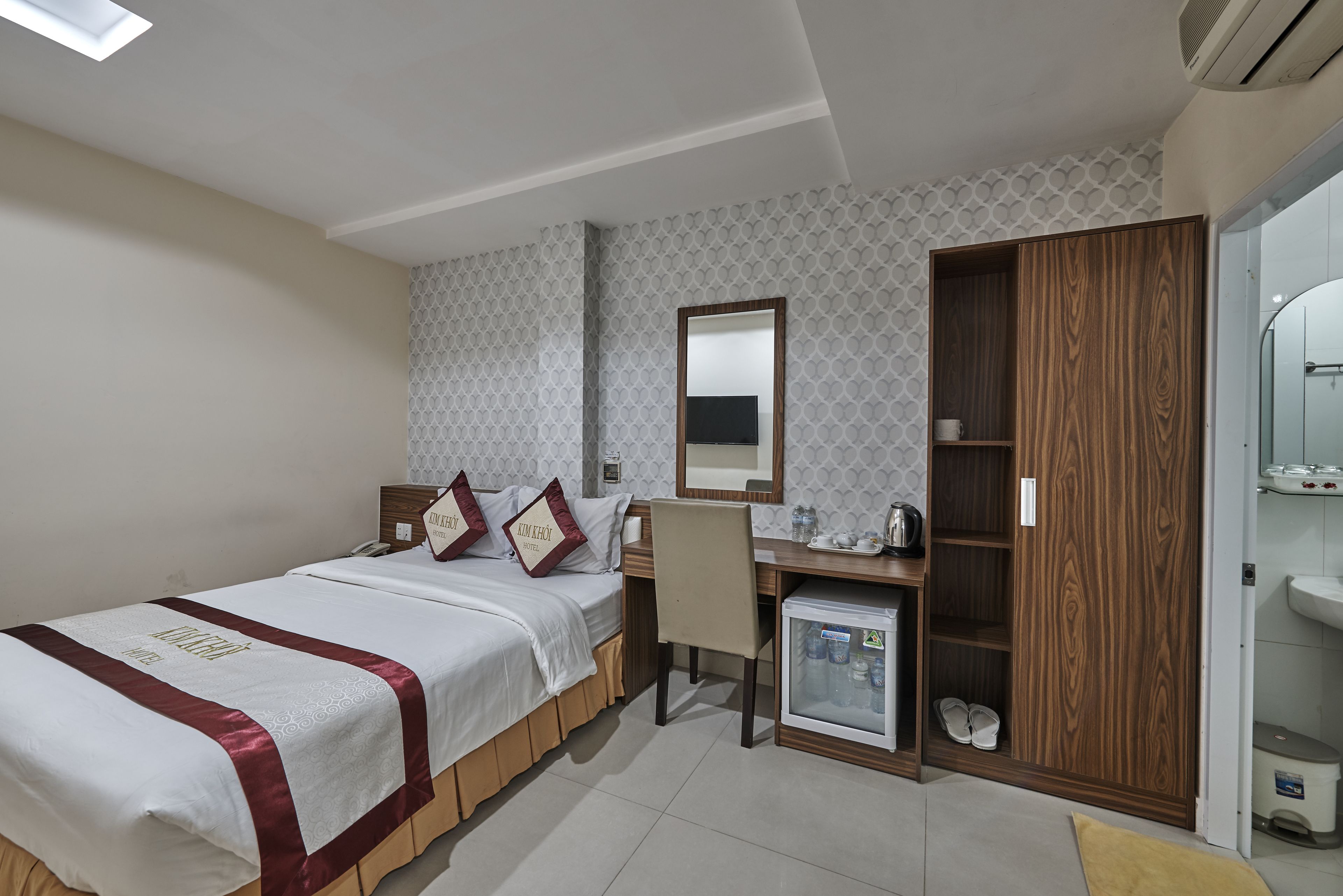 A hotel room with a bed, a desk, a mirror, a wardrobe, and a mini fridge.