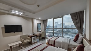 Habitación de hotel con dos camas, un escritorio, una silla, un televisor y un ventanal con vista a la ciudad.
