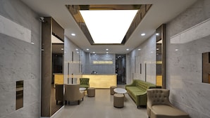 Un moderno hall de hotel con mostrador de recepción, sofás verdes y un techo alto con luz natural.