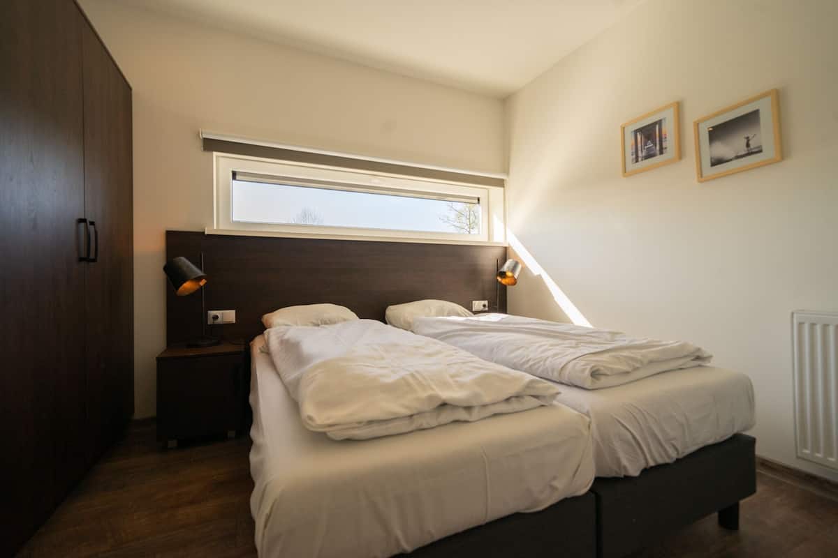 A bedroom with two beds, a window, a nightstand, a lamp, and a wardrobe.