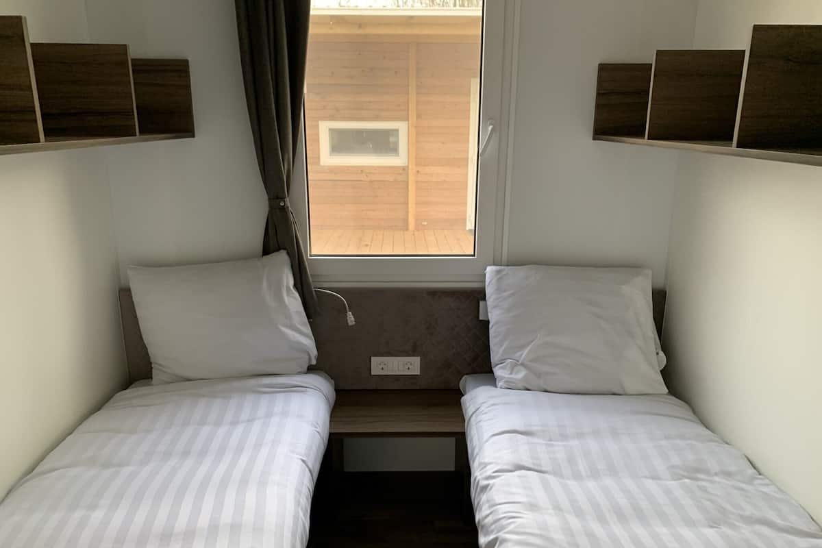 A small, compact room with two single beds, a window, and a wooden floor.