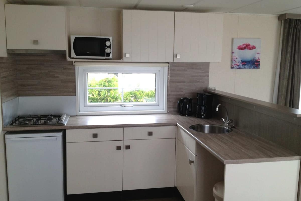 A compact kitchen with a microwave, stove, and sink, a window with a view of greenery, and a coffee maker.