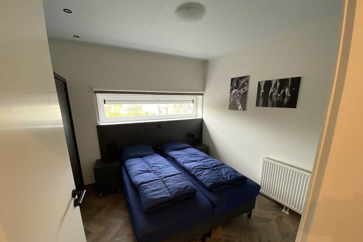 A bedroom with two beds, a window, a radiator, and a door.