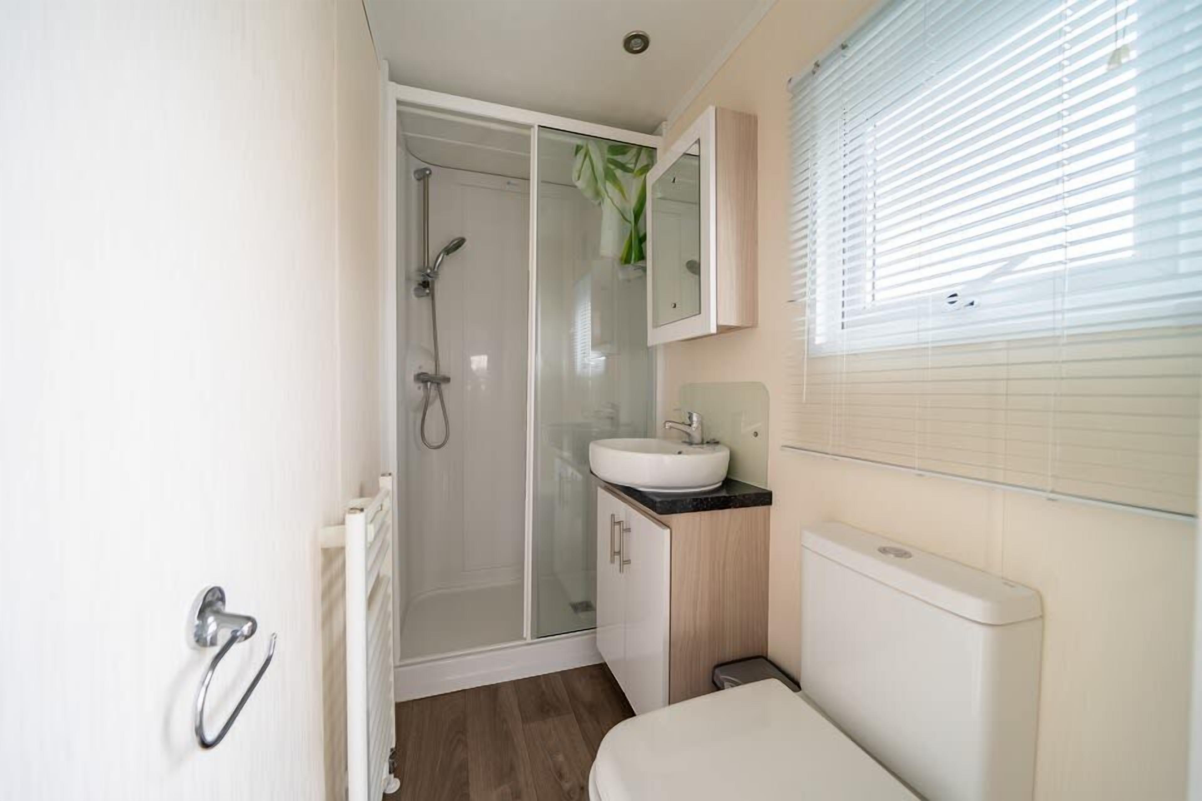 Een moderne badkamer met een douchecabine van glas, een witte wastafel en een toilet.