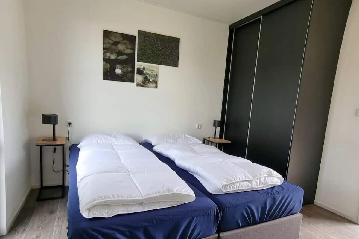 A double bed with white and blue bedding, two bedside tables with lamps, and a dark sliding door.
