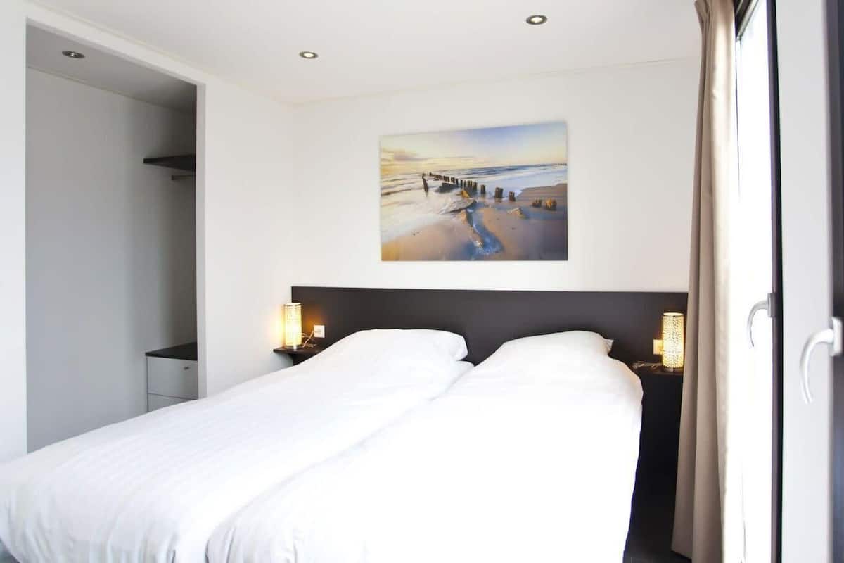 A hotel room with a bed, a painting on the wall, and a window with curtains.