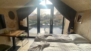 Una habitación pequeña y acogedora con una cama, un escritorio y una silla. Hay un ventanal con cortinas y vistas al exterior.