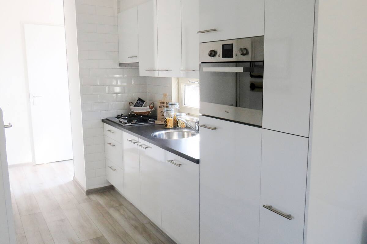 A modern kitchen with white cabinets, a stainless steel sink, and a built-in oven.