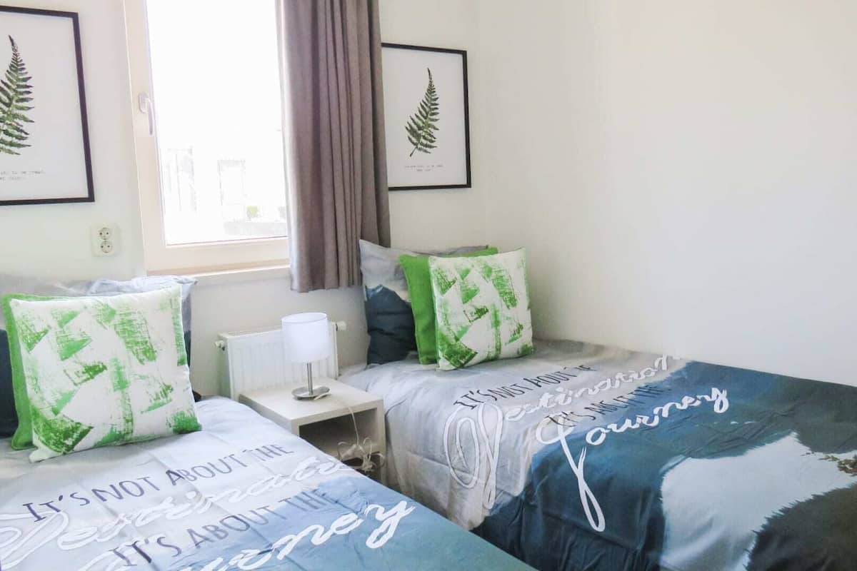 A bedroom with two beds, a bedside table with a lamp, and framed botanical prints on the wall.