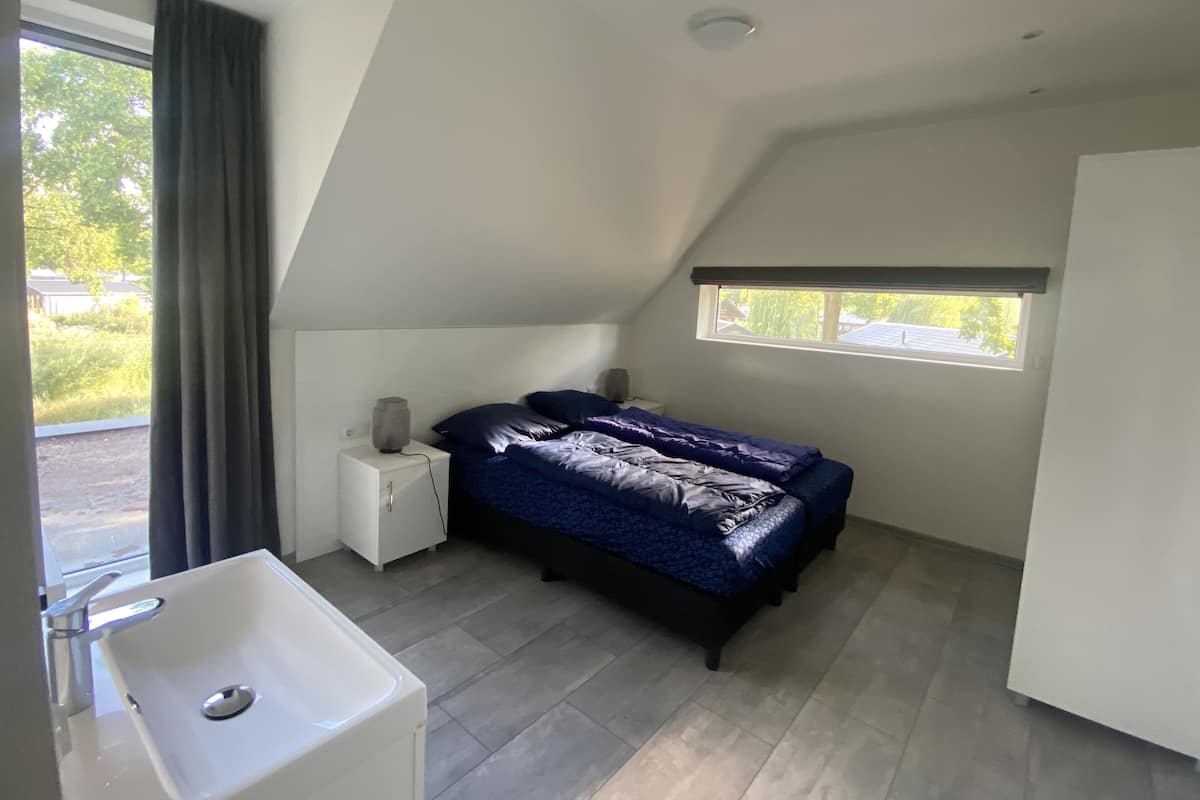 A bedroom with a bed, a nightstand, a lamp, a window, and a bathroom with a sink.