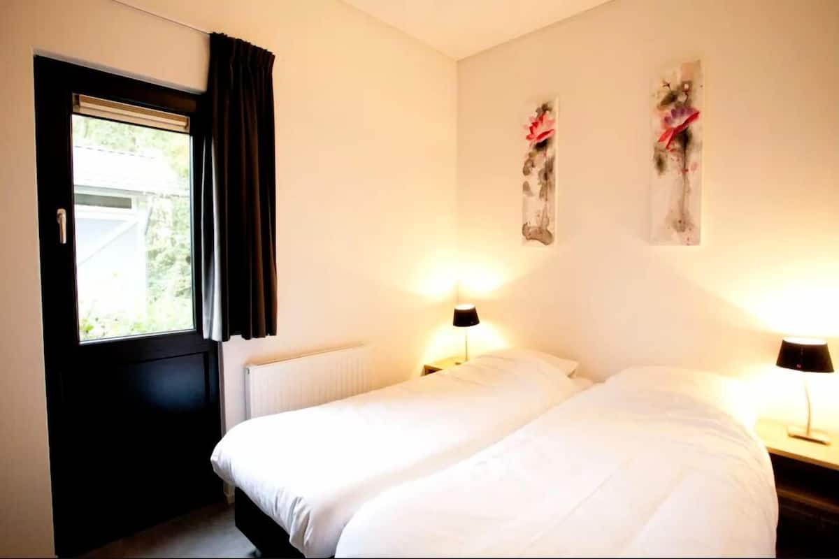 A room with two beds, a window with curtains, a radiator, and two wall-mounted lamps.