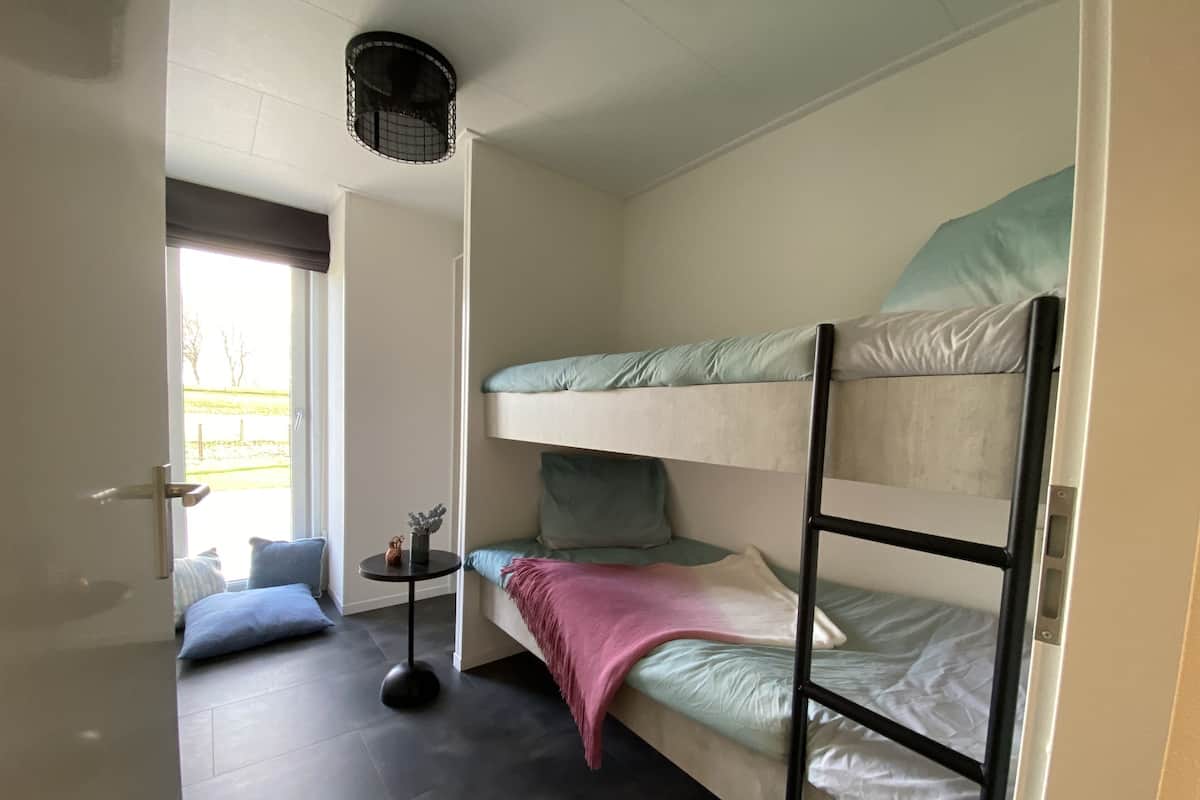 A bunk bed room with a small table and a chair, a door leading outside, and a ceiling light fixture.