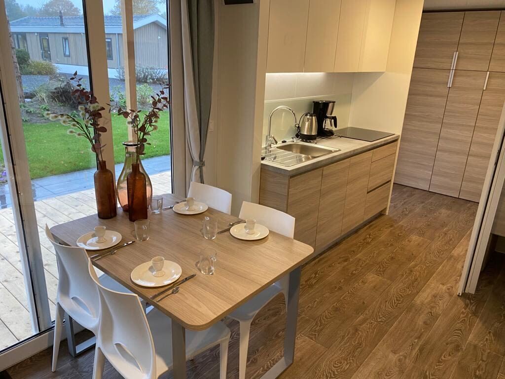 Een moderne keuken met een houten aanrecht, een spoelbak en een koffiezetapparaat. Er staat een eettafel met stoelen en een vaas met bloemen.