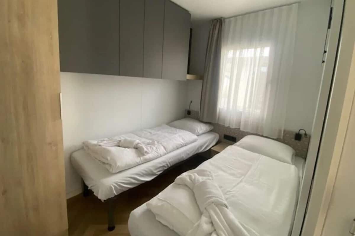 A bedroom with two single beds, a wooden wardrobe, and a window with sheer curtains.