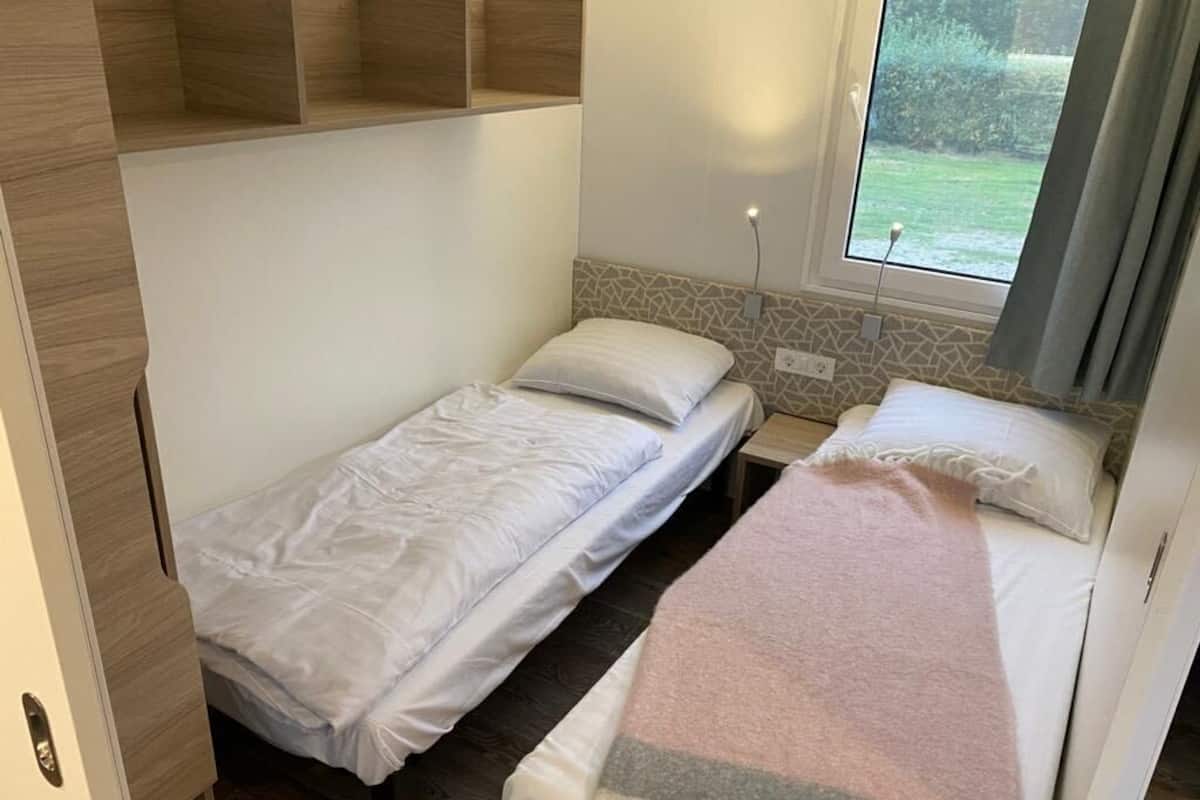 A compact room with two single beds, a small table, and a window with a view of greenery.