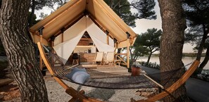 Una tienda de campaña acogedora al aire libre con una hamaca, una terraza de madera y una pequeña kitchenette.