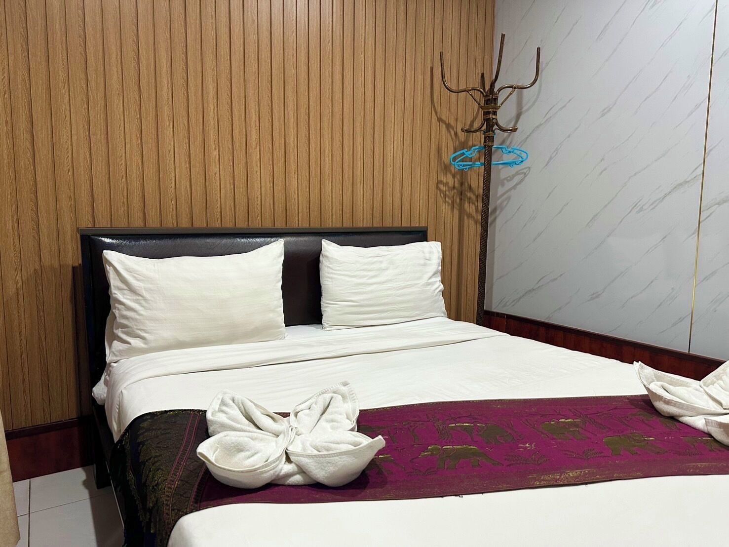 A hotel room with a wooden paneled headboard, a bed with white linens, and a purple throw blanket.