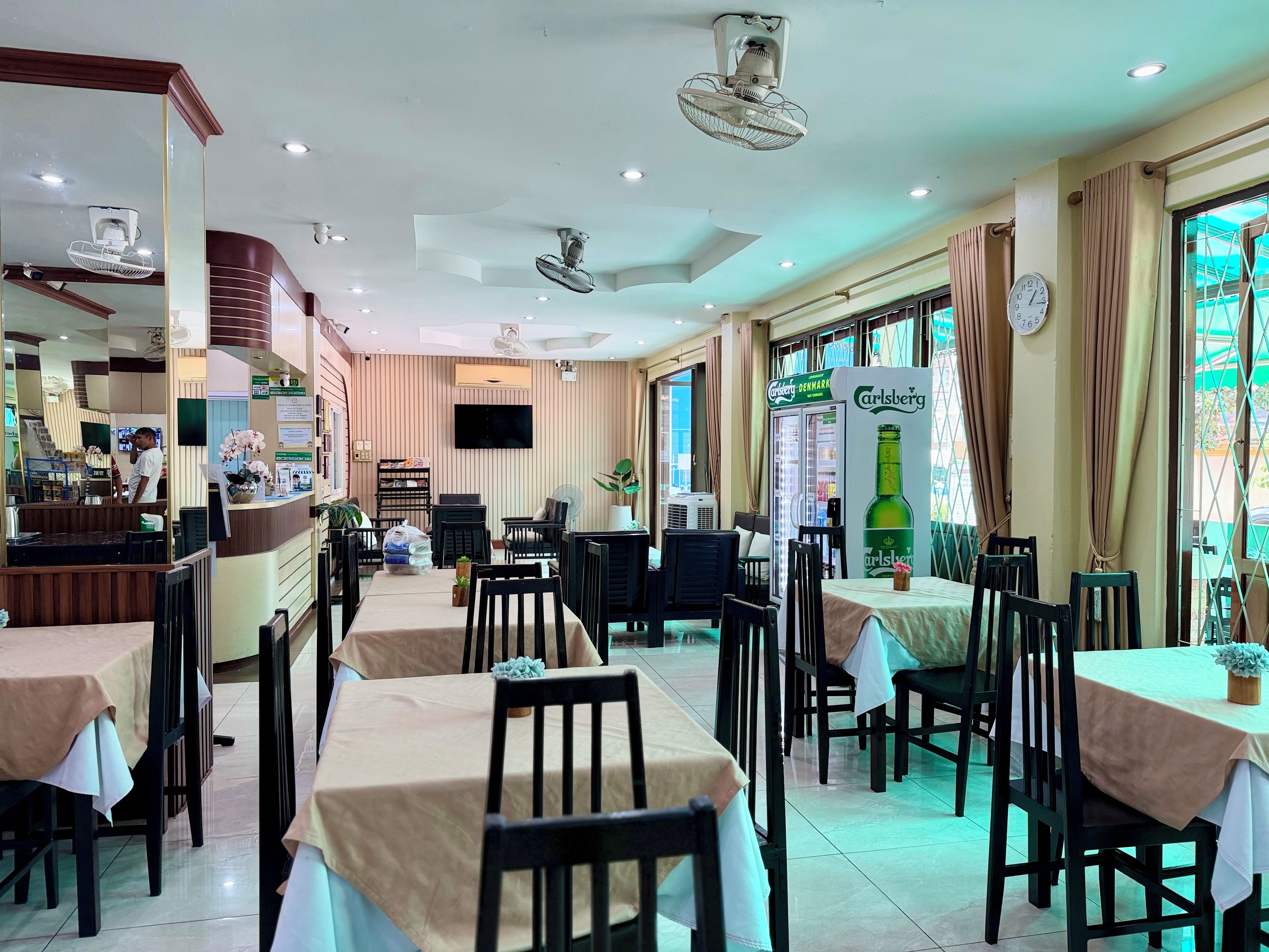 A restaurant with multiple tables, chairs, ceiling fans, and a large window with curtains.