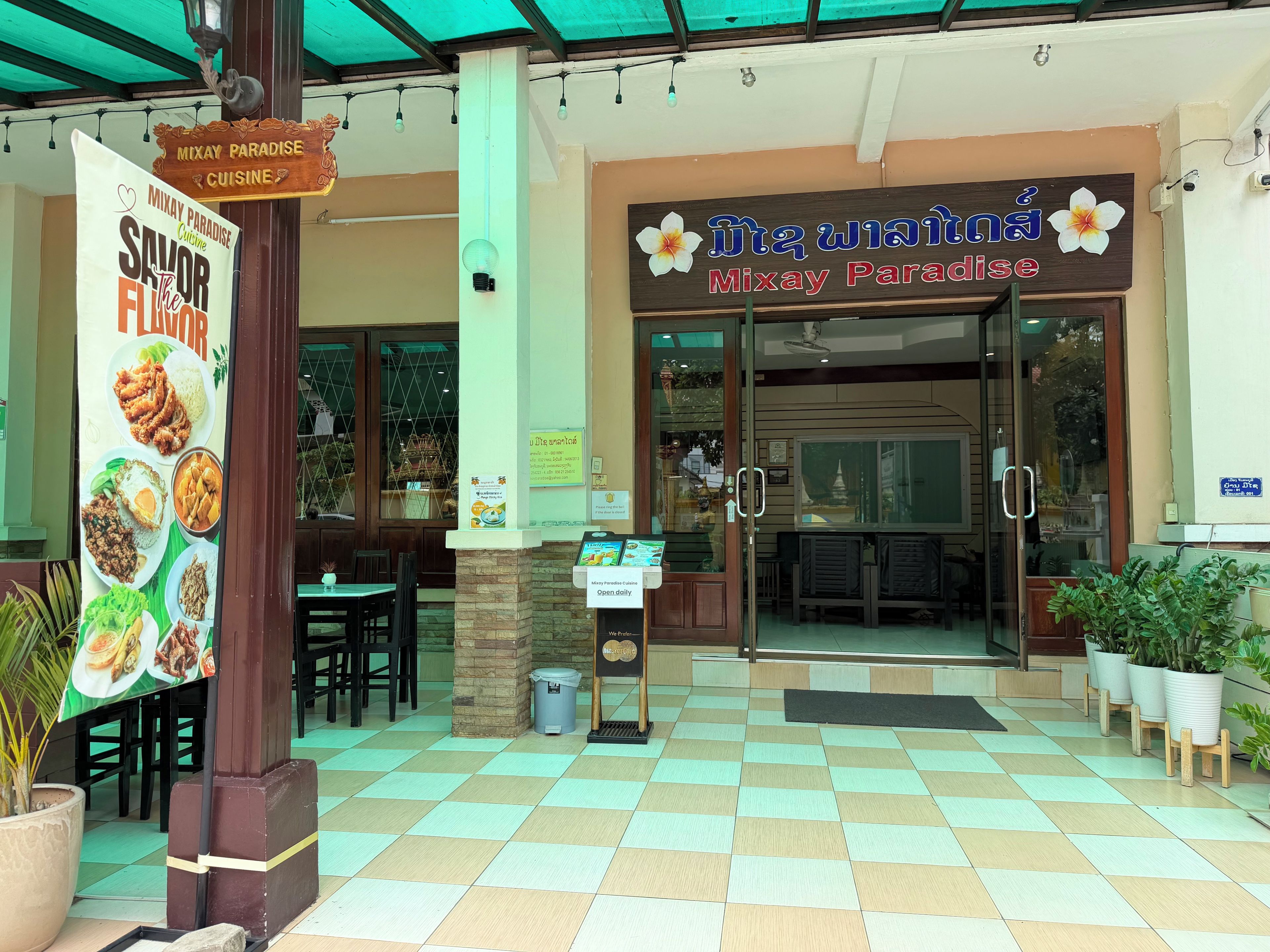 L’entrée d’un restaurant, avec une enseigne, un espace extérieur aménagé pour les clients et un sol carrelé.