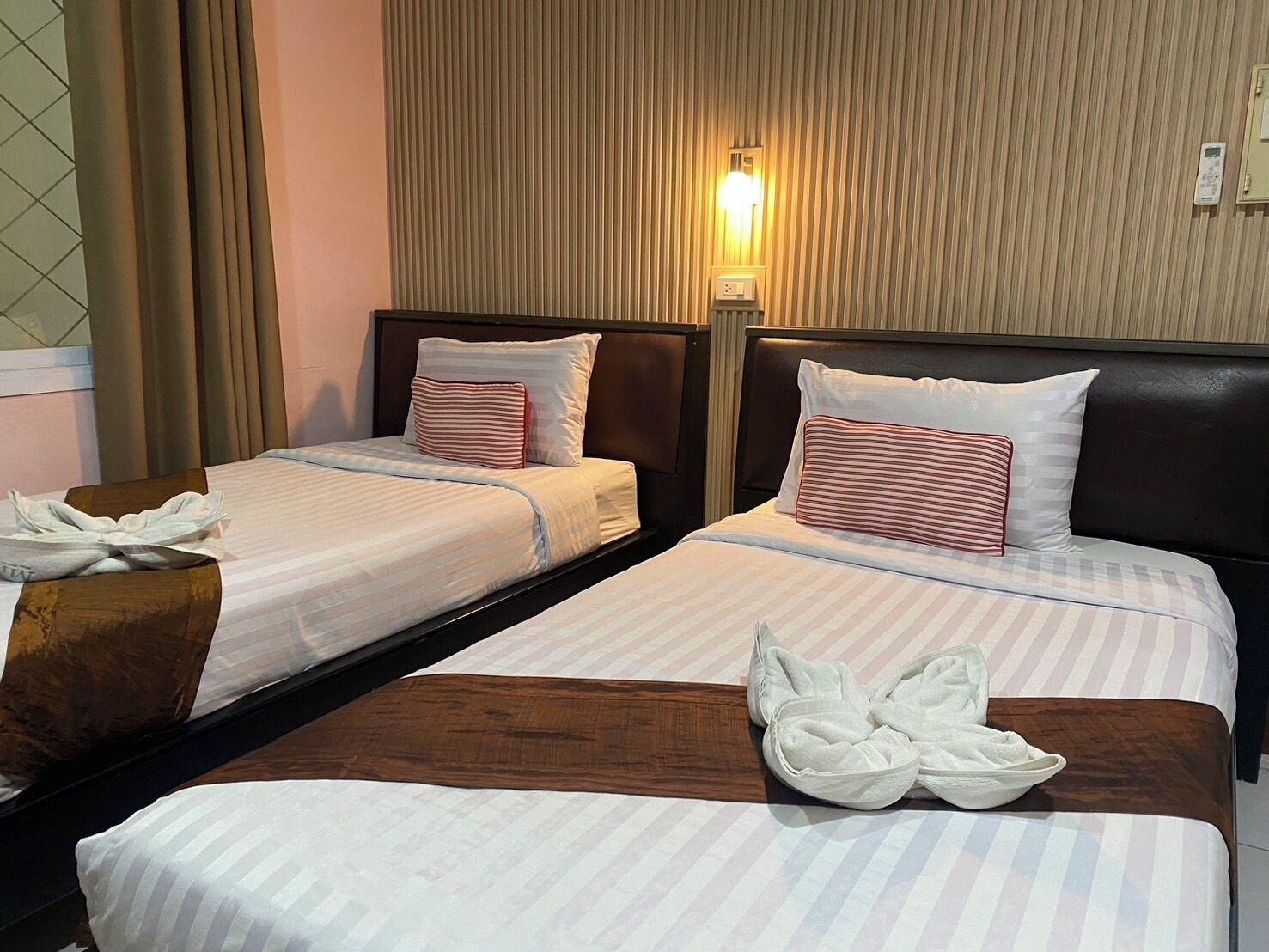 Une chambre d’hôtel avec deux lits, chacun doté de draps et d’oreillers à rayures, d’une tête de lit en bois, d’une table de chevet avec une lampe et d’une petite table de nuit en bois.