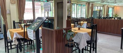 A restaurant with multiple tables and chairs, a menu stand, and a decorative plant.
