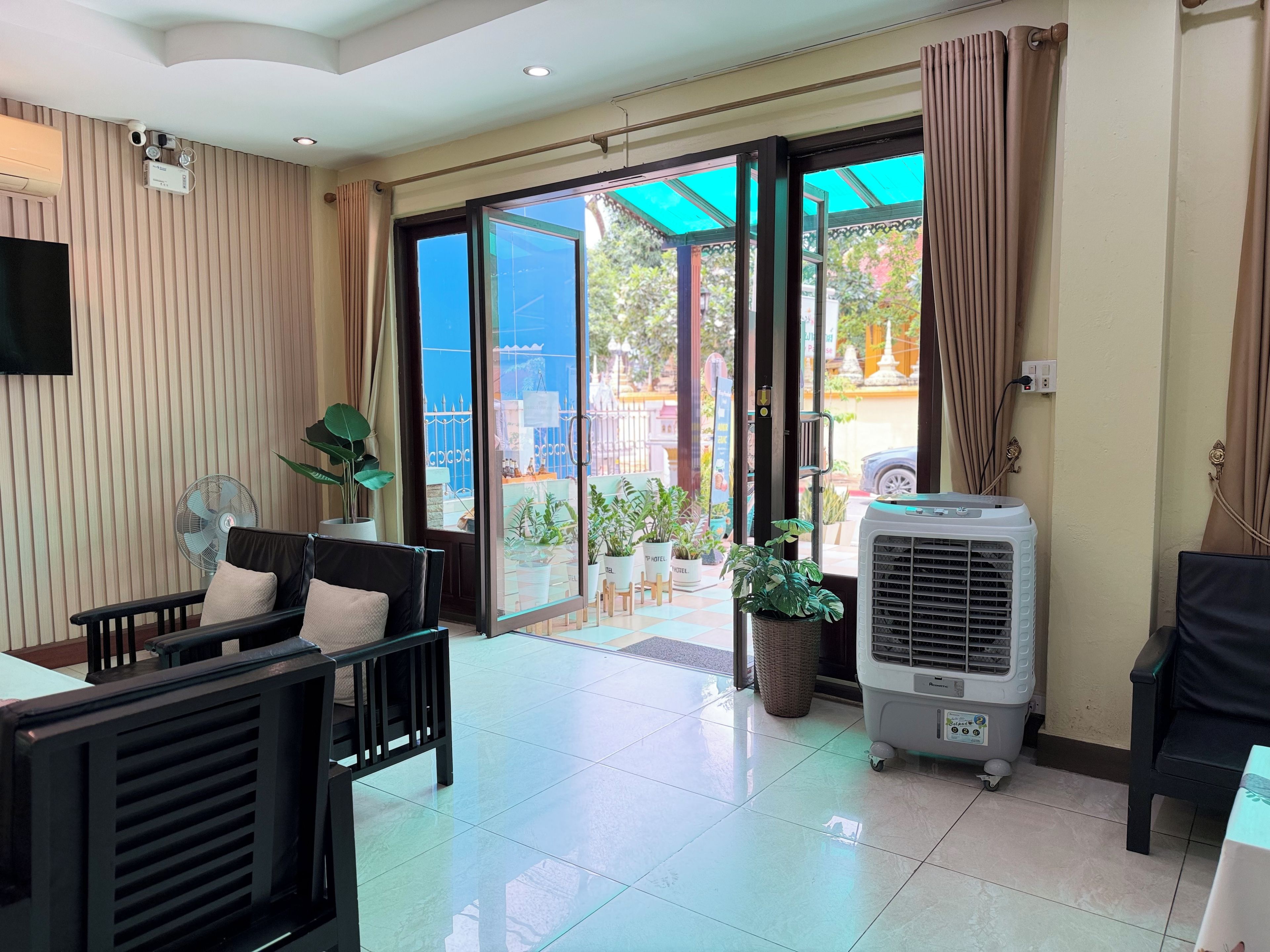 Une chambre d’hôtel avec une porte-fenêtre coulissante donnant sur l’extérieur, un ventilateur de plafond, une table avec des chaises et une plante en pot.