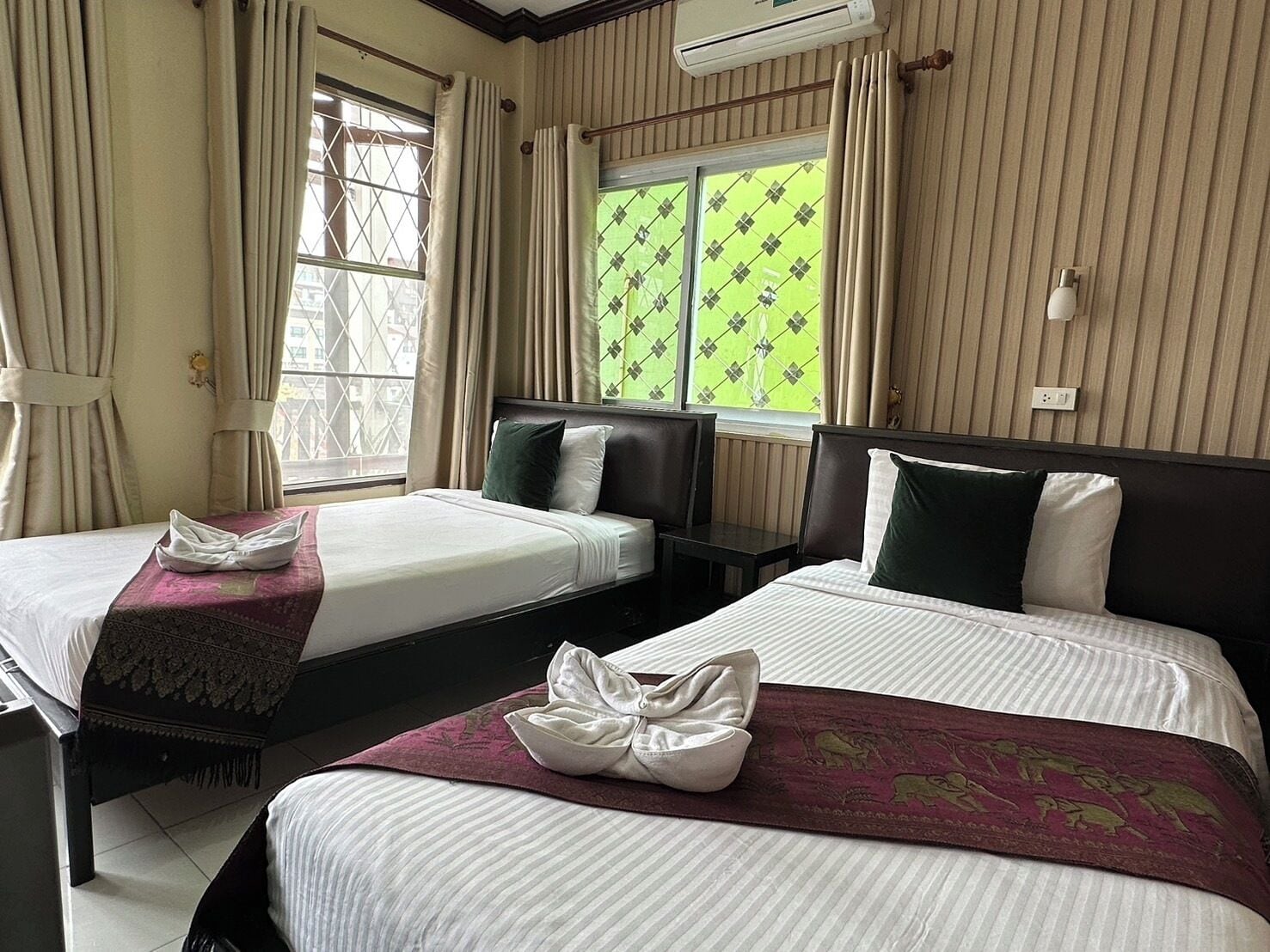 A hotel room with two beds, a window with a view, and an air conditioning unit.