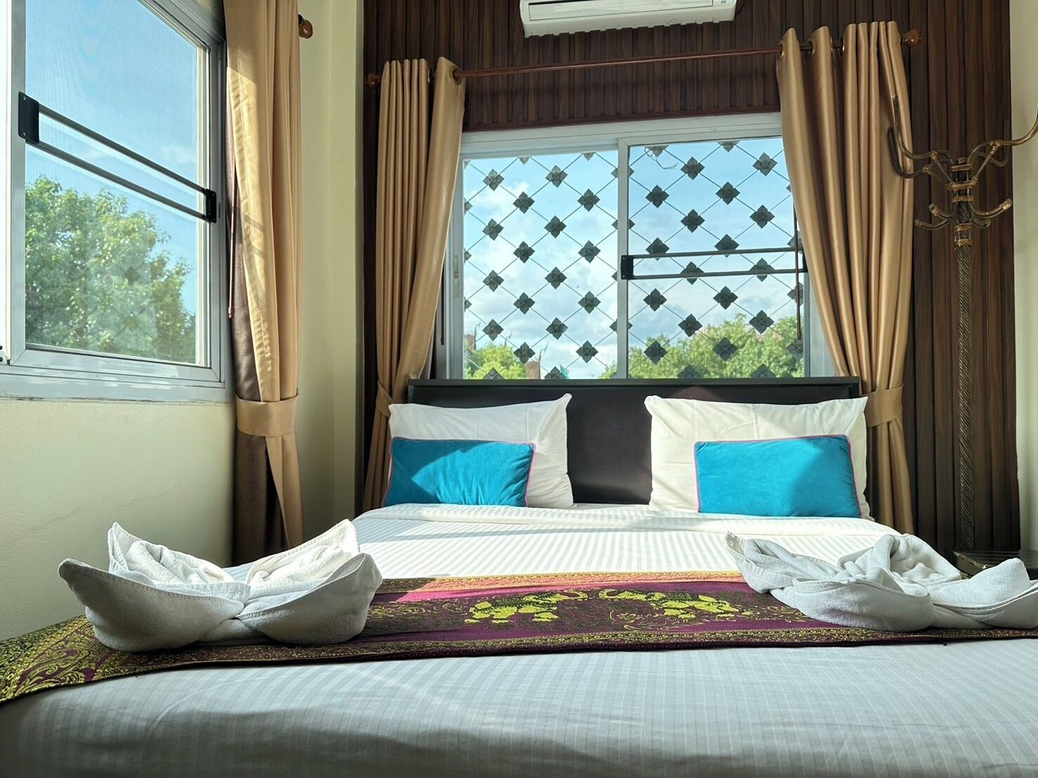 A neatly made bed with white and blue pillows, a patterned throw, and a window with curtains.