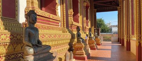 Una serie de estatuas de Buda sentadas en un corredor cubierto con detalles arquitectónicos dorados y rojos ornamentales.