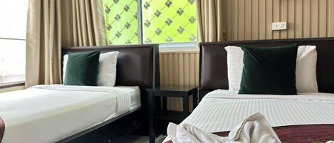 A hotel room with two beds, a window with patterned curtains, a bedside table, and a towel on the floor.