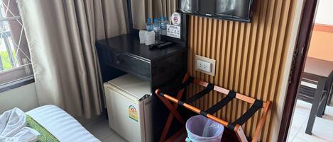 A hotel room with a bed, a desk with a television, a small refrigerator, a wooden chair with a tray, and a window with curtains.