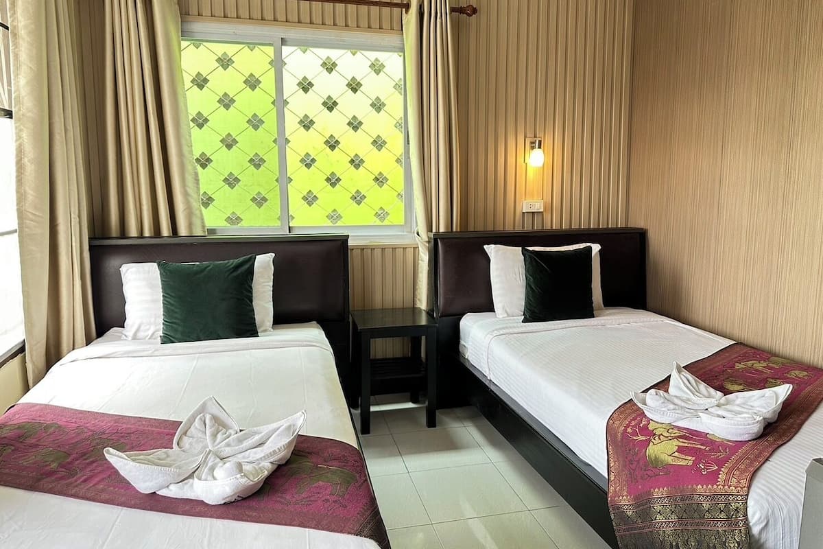 A hotel room with two beds, a window with curtains, a bedside table, and a wall-mounted air conditioner.