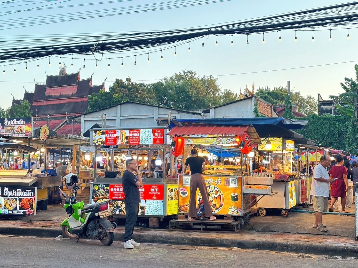 Un marché de stands de nourriture de rue, avec une moto garée sur le côté.