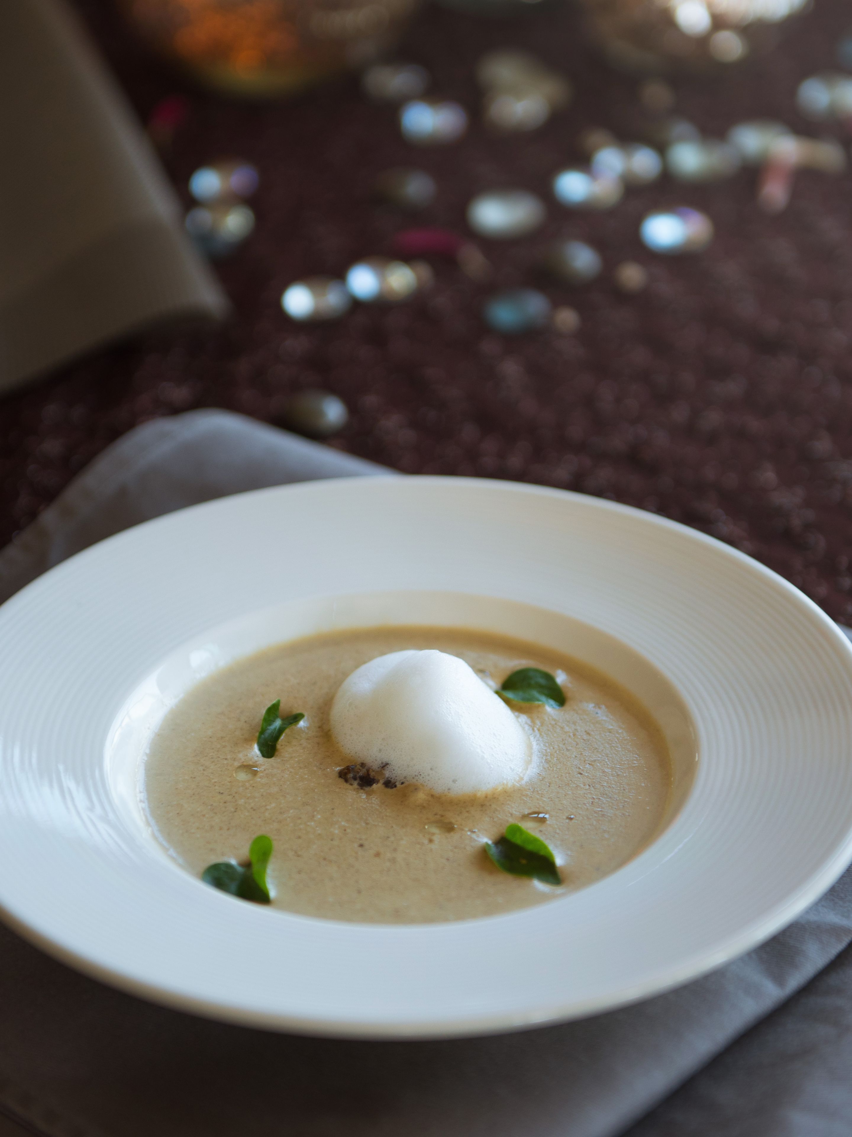 A white plate with a creamy soup and a poached egg, garnished with green leaves, on a dark surface.