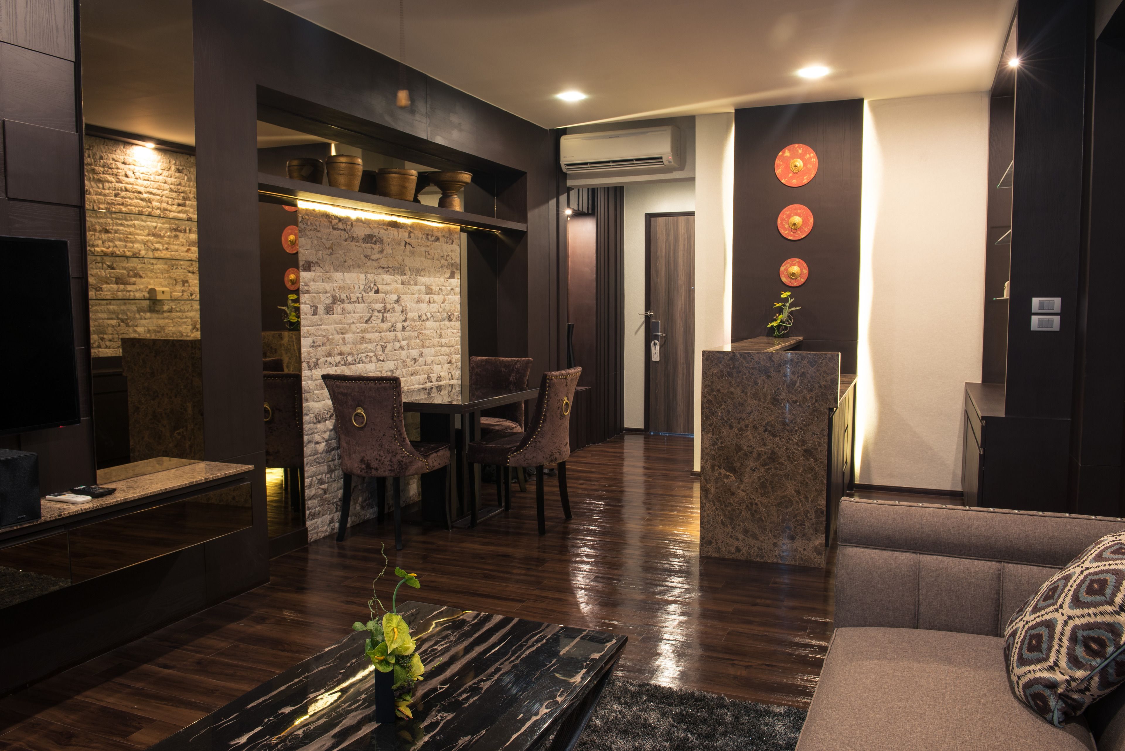 A modern living room with a stone wall, dark wooden flooring, and a seating area with a sofa and chairs.