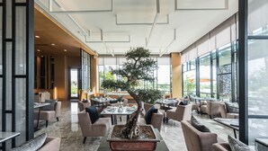 A modern indoor space with a central bonsai tree, comfortable seating, and large windows. - North Hill City Resort (Hang Dong)