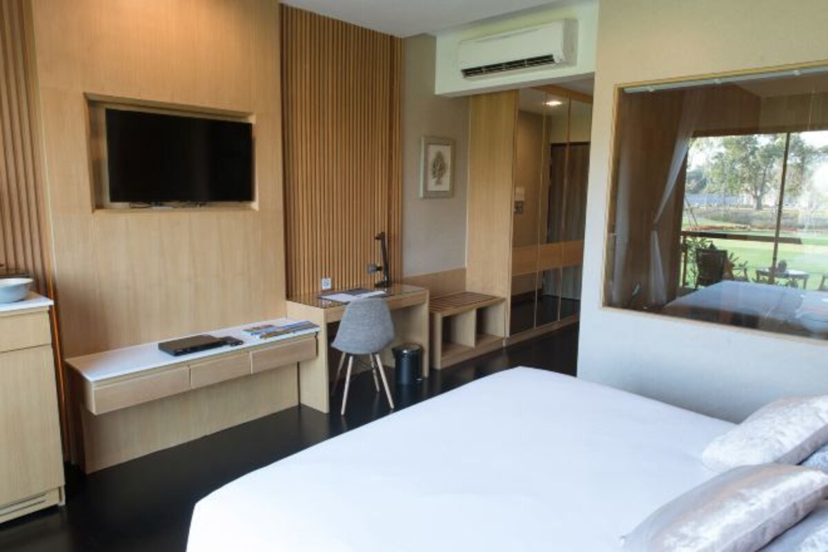 Una habitación de hotel moderna con cama, escritorio, silla, televisor y un ventanal amplio.